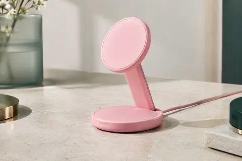 Chargeur sans fil Google Pixelsnap rose bonbon installé sur son support, posé sur une surface minérale claire.