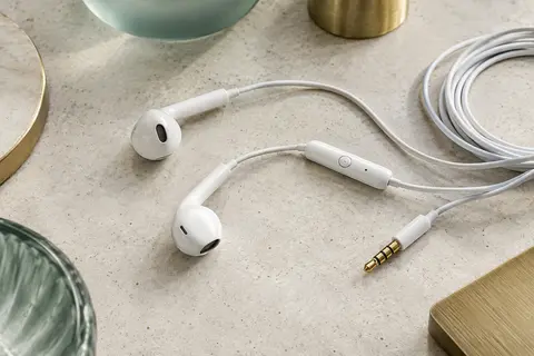Écouteurs filaires blancs avec microphone et télécommande à un bouton posés sur une surface claire
