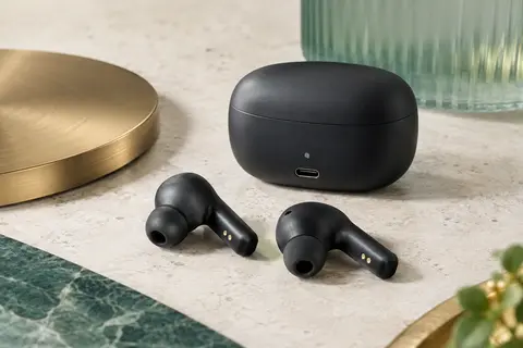Écouteurs intra-auriculaires noirs avec embouts en silicone et étui de recharge sur une surface minérale claire.