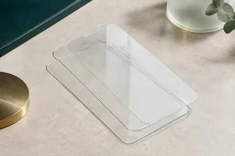 Trois protections d’écran transparentes en verre trempé disposées sur une surface minérale claire.