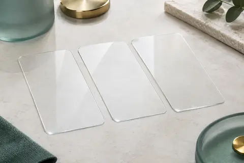 Trois protections d’écran transparentes en verre trempé pour iPhone 14 sur une surface minérale claire.