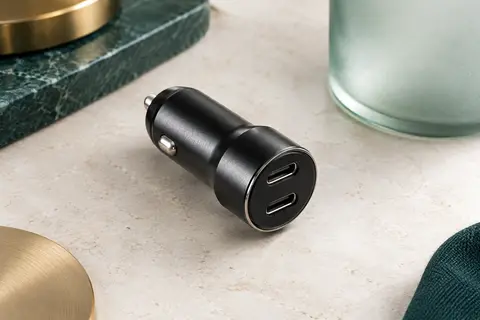 Chargeur voiture compact en métal noir avec deux ports USB-C, posé sur une surface minérale claire