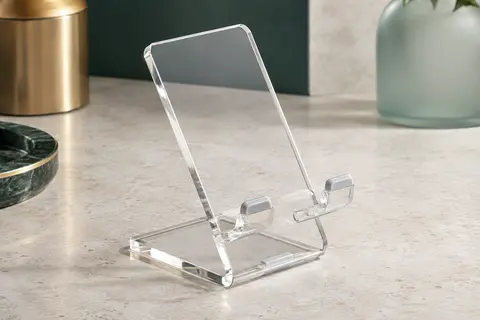 Support de téléphone de bureau en acrylique transparent posé sur une surface minérale claire.