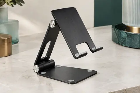 Support de bureau pliable noir en aluminium brossé, posé ouvert sur une surface minérale claire
