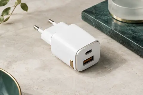 Chargeur secteur blanc à deux ports, USB-C et USB-A, posé sur une surface minérale claire.