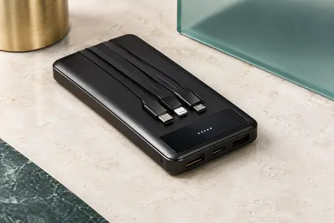 Batterie externe noire avec quatre câbles intégrés, ports USB et écran LED sur une surface claire.